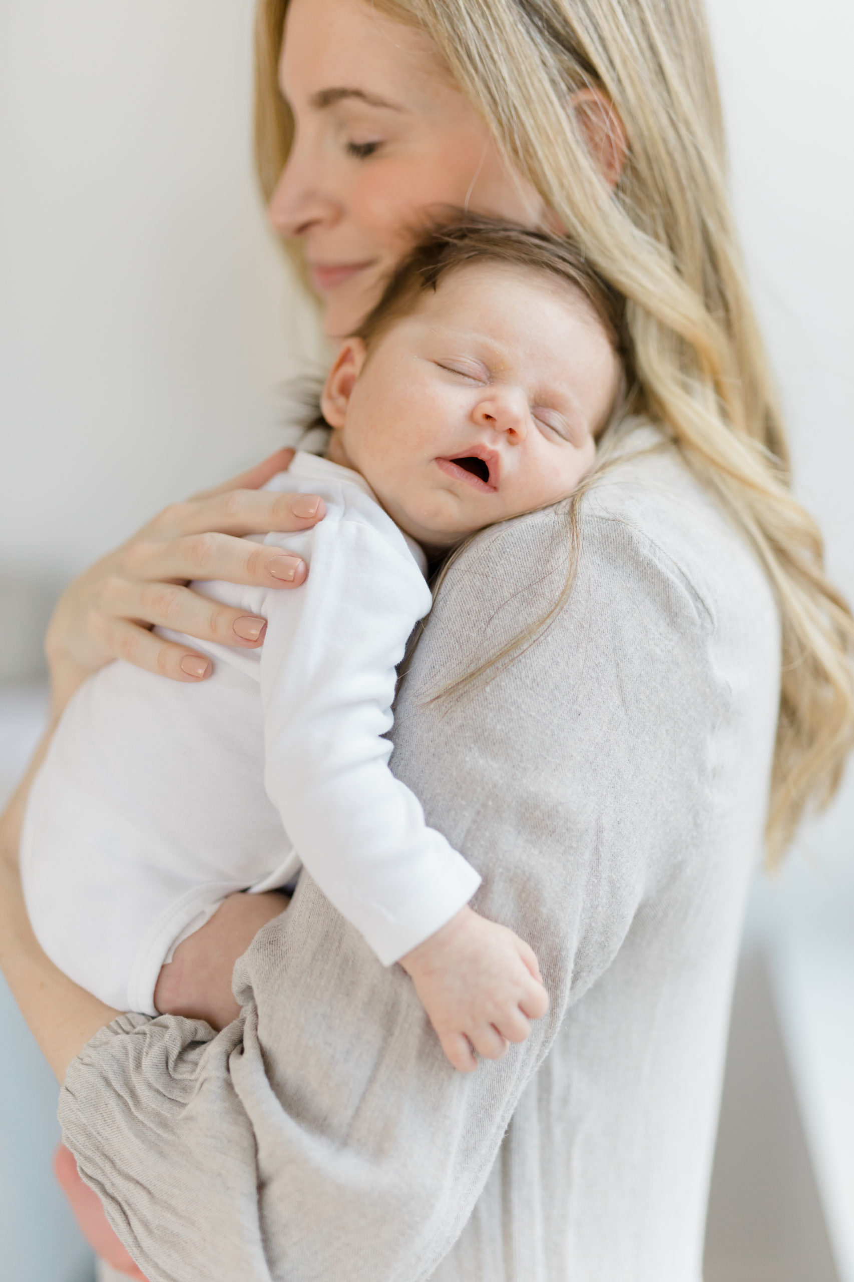 A close up of a sleeping baby in her mom's arms at an in home newborn photography session in NYC photographed by Jacqueline Clair Family Photography. 