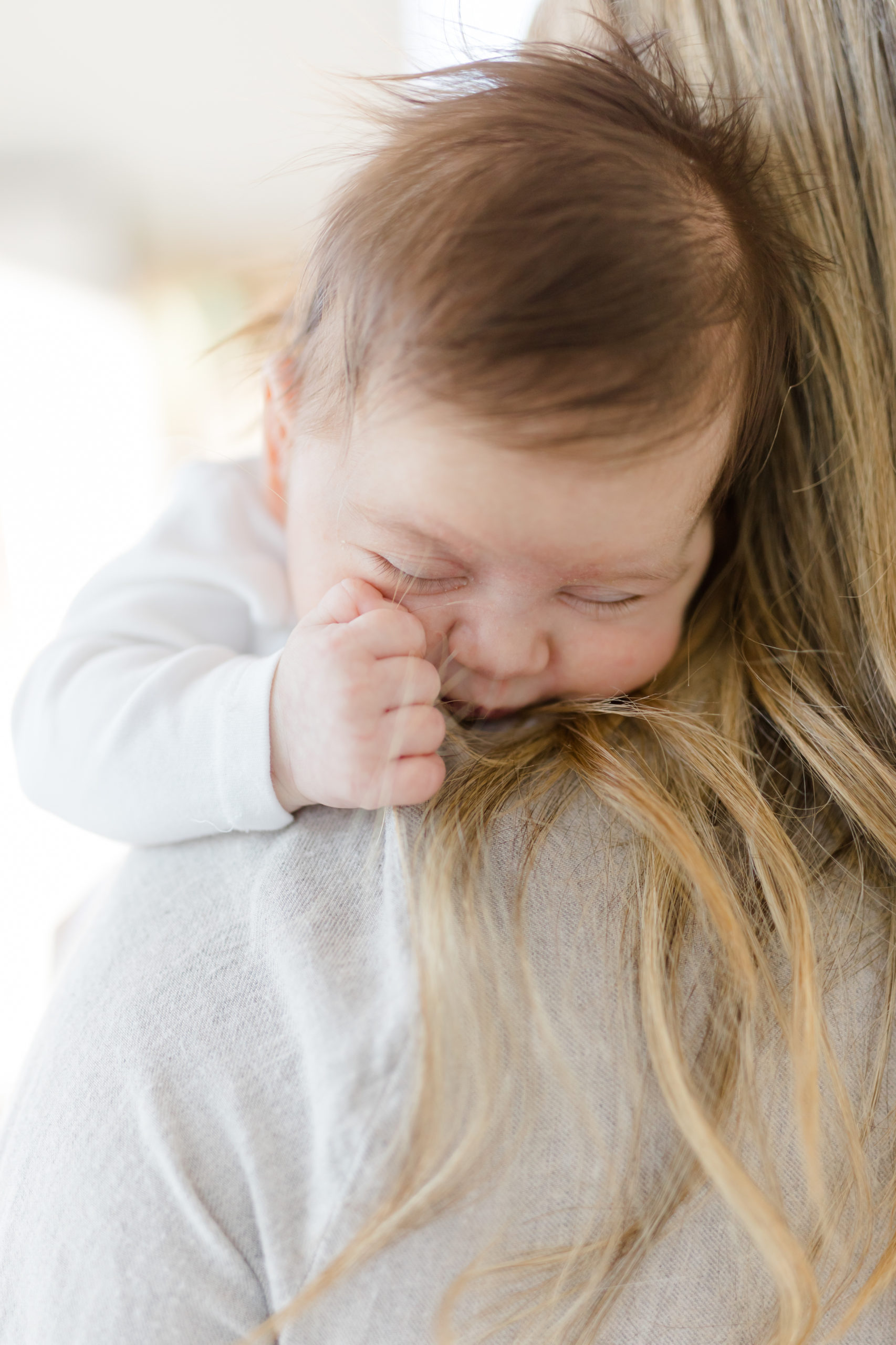 A close up of a baby clutching her mom's hair at an in home newborn photography session in NYC photographed by Jacqueline Clair Family Photography. 