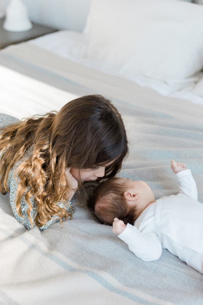 A young girl cuddles with her baby sister at an in home newborn photography session in NYC photographed by Jacqueline Clair Family Photography. 