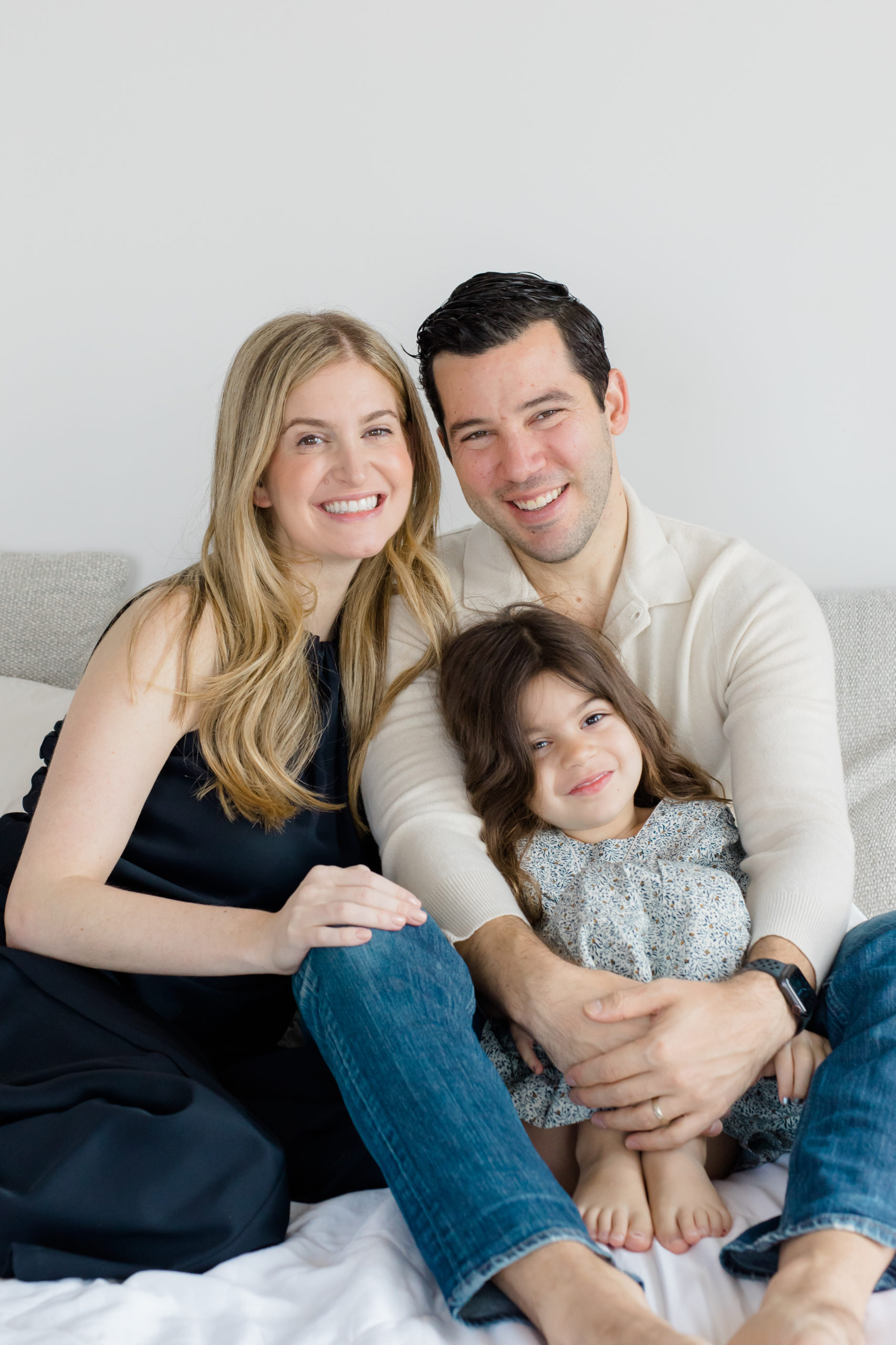 A mom, dad, and toddler on their bed at an in home newborn photography session in NYC photographed by Jacqueline Clair Photography. 