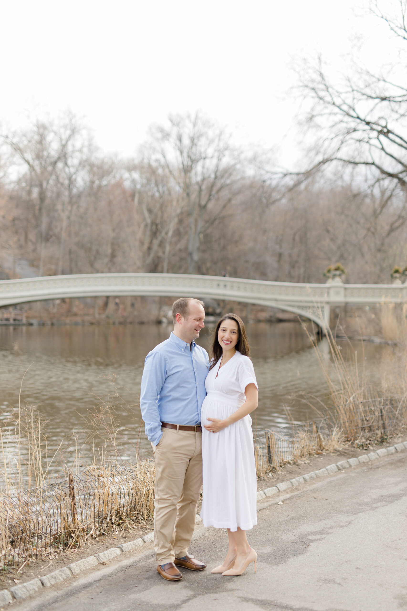 An expecting couple in front of ow Bridge in Central Park during a New York City maternity photography session with Jacqueline Clair Photography