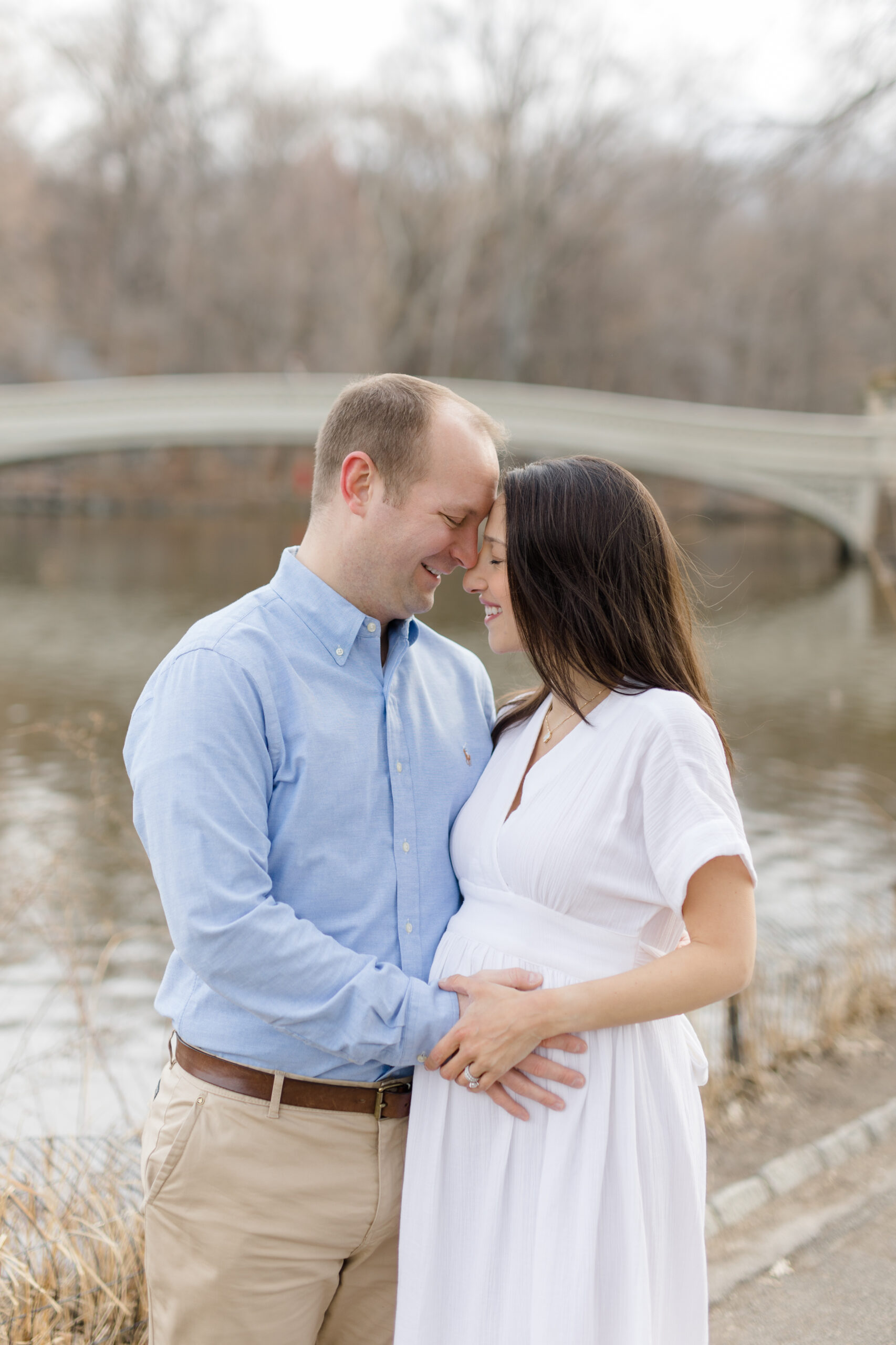 An expecting couple together in front of Bow Bridge in Central Park during a New York City maternity photography session with Jacqueline Clair Photography