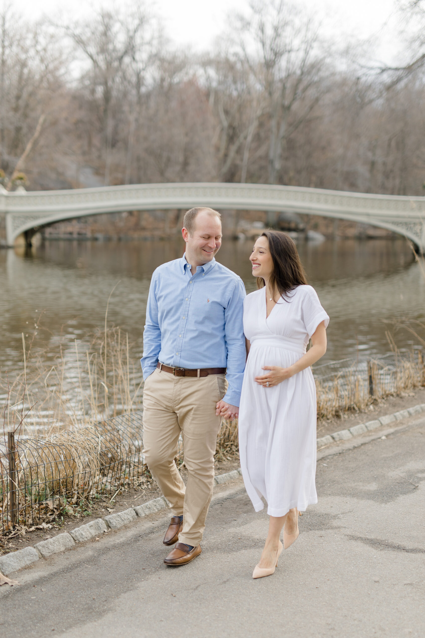 An expecting couple walk together in Central Park during a New York City maternity photography session