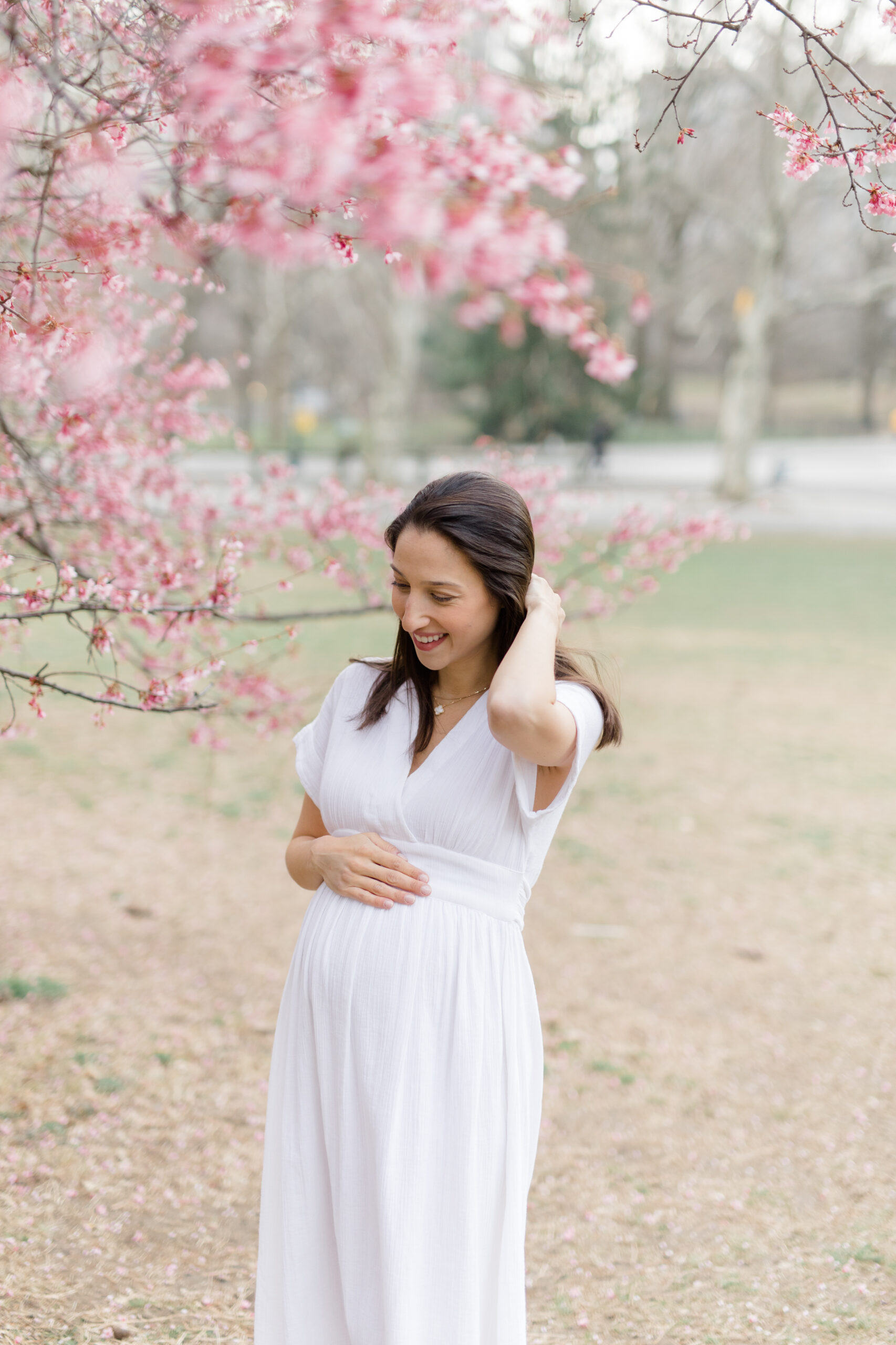 A pregnant woman in front of a pink flowering tree at a New York City maternity photography session with Jacqueline Clair Photography