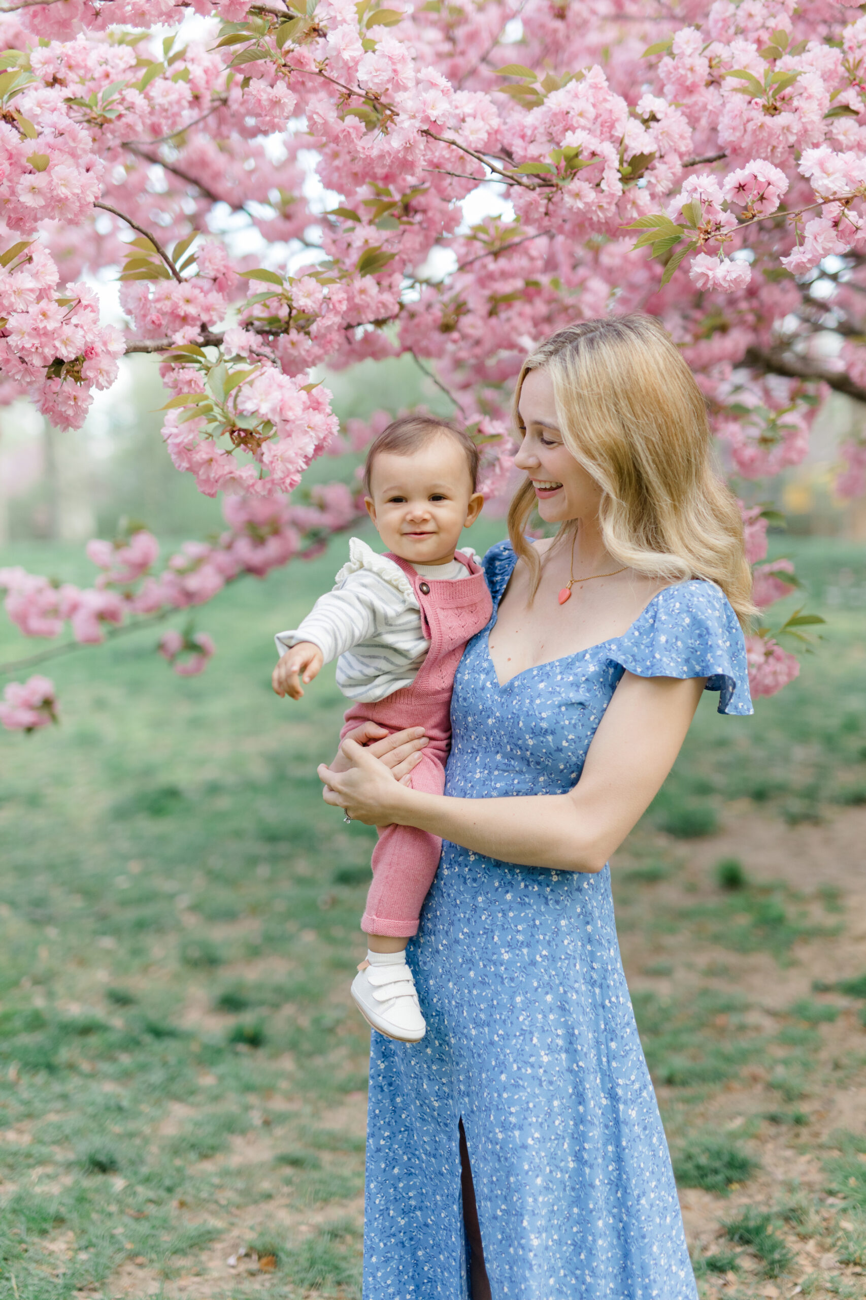 A mom holds her baby in the cherry blossoms at a spring family mini session in Central Park shot by Jacqueline Clair Photography
