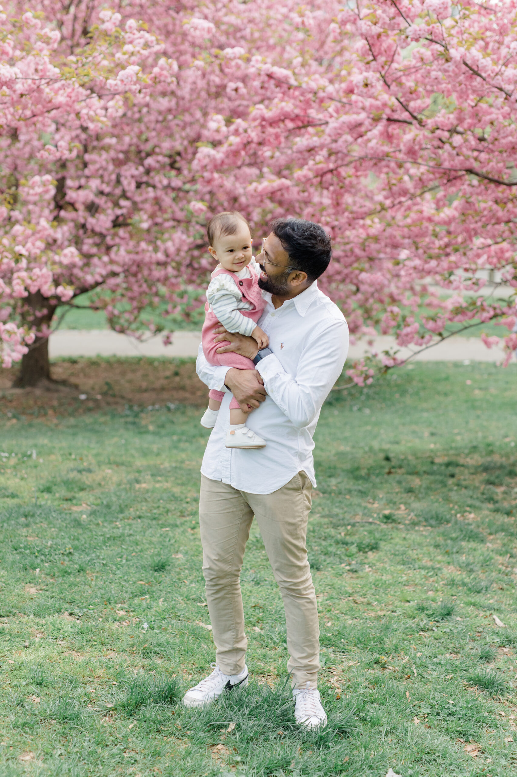 A dad holds his baby in the cherry blossoms at a spring family mini session in Central Park shot by Jacqueline Clair Photography