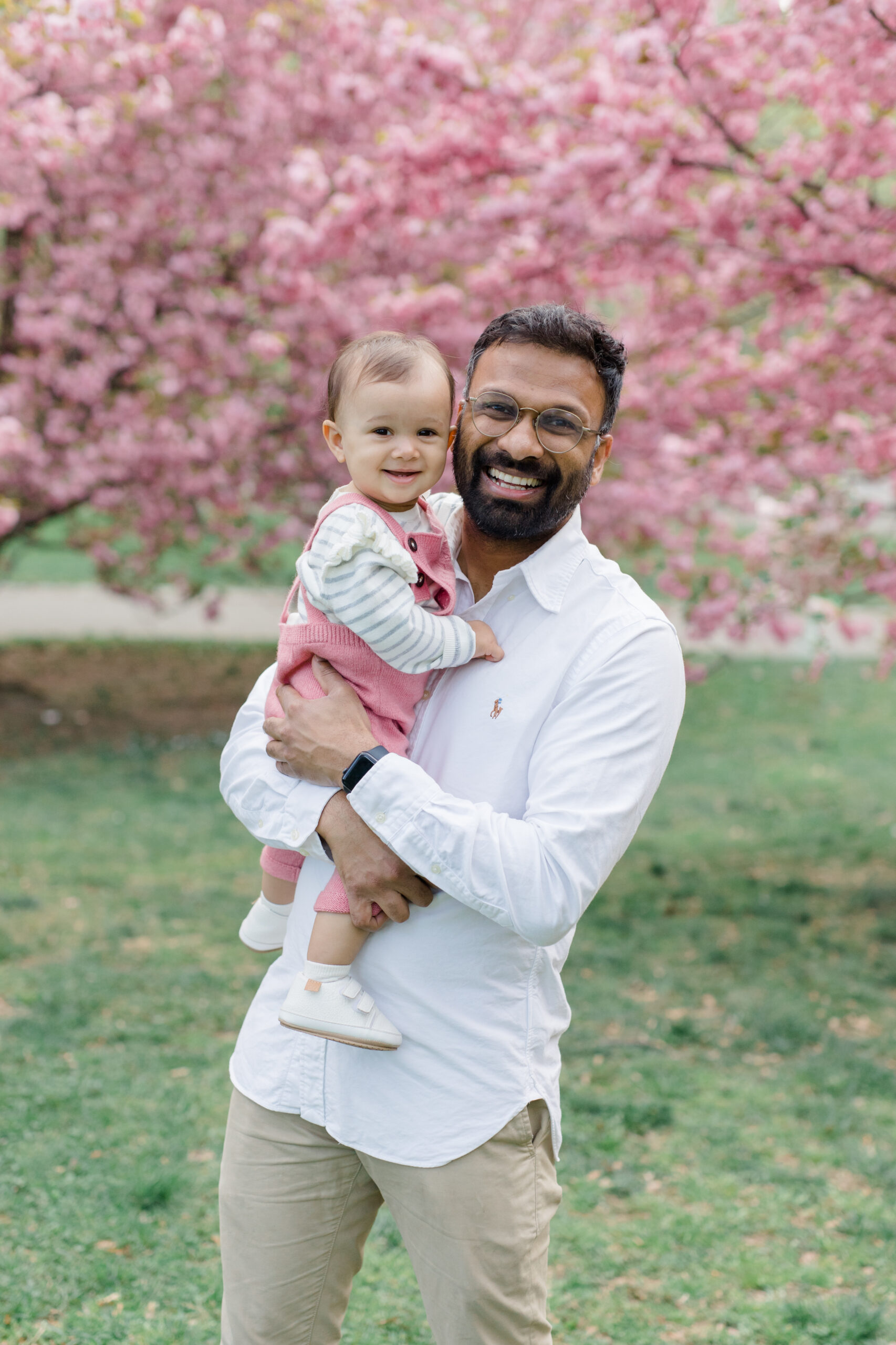 A dad holds his baby in the cherry blossoms at a spring family mini session in Central Park shot by Jacqueline Clair Photography