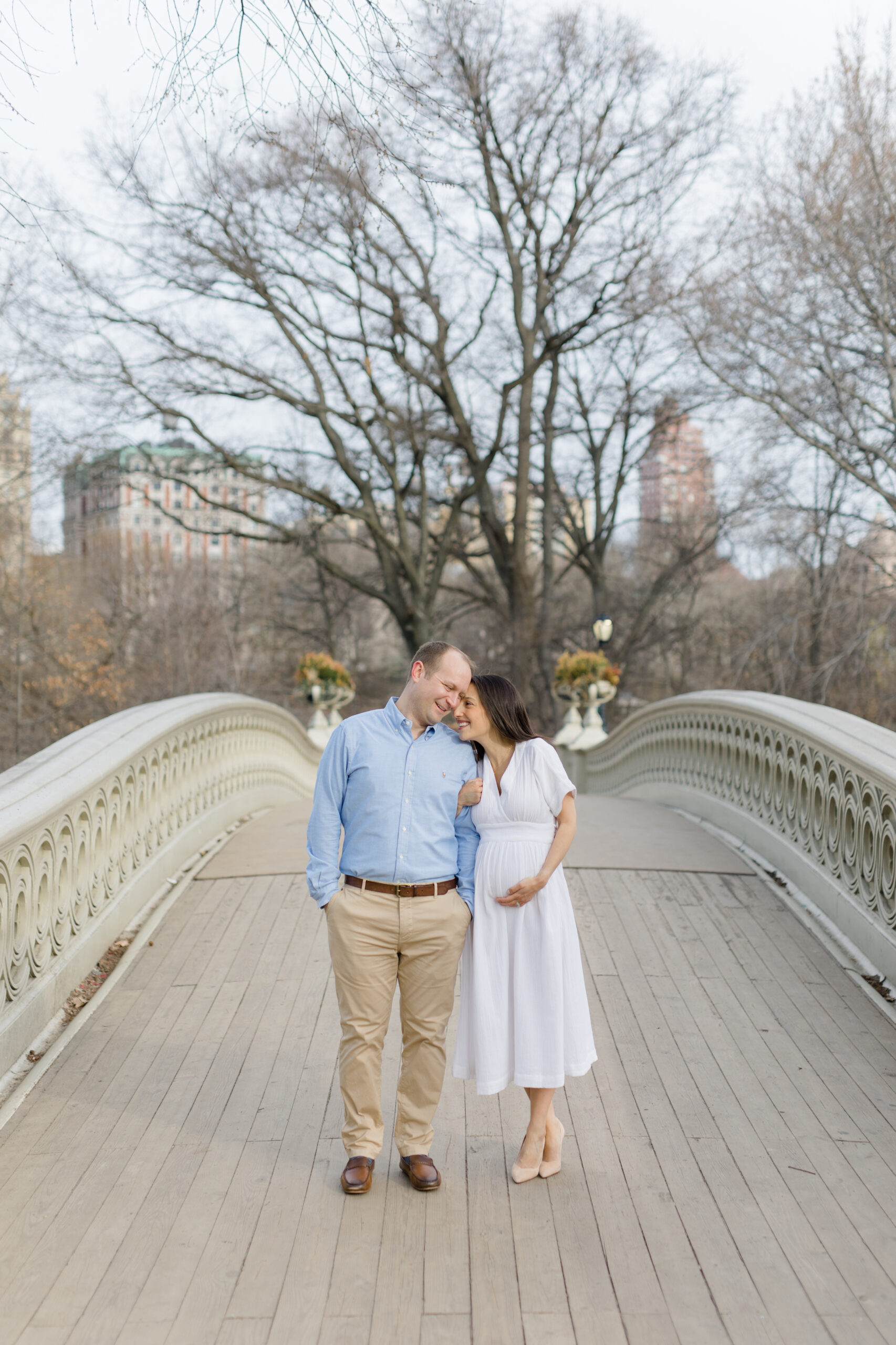 An expecting couple cuddle together in Central Park during a New York City maternity photography session with Jacqueline Clair Photography