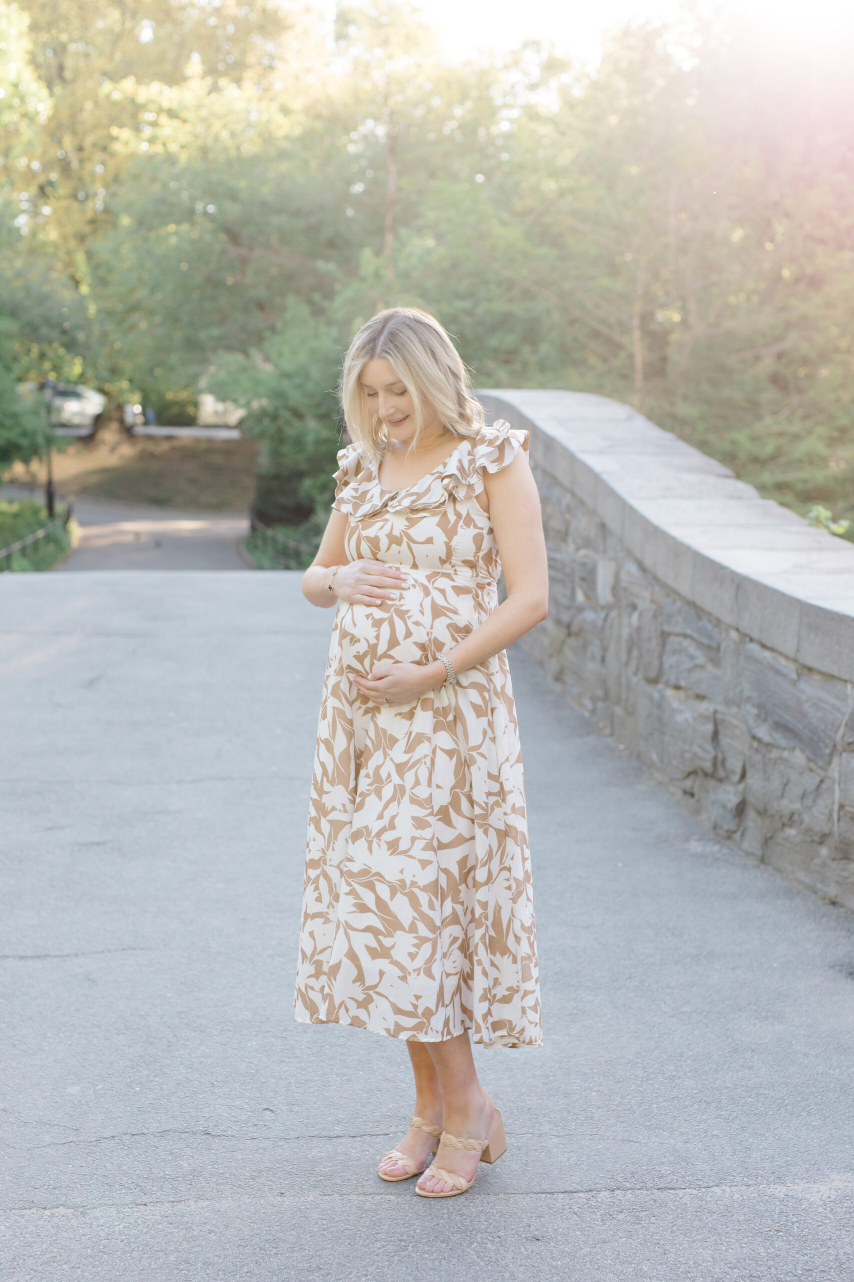 An expecting mom looks at her baby bump on Gapstow Bridge at a maternity photo session in Central Park shot by Jacqueline Clair Photography