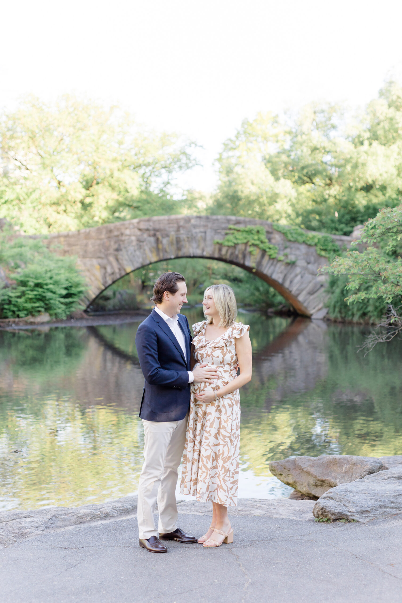 A pregnant woman and her husband smile at each other at a maternity photo session in Central Park shot by Jacqueline Clair Photography