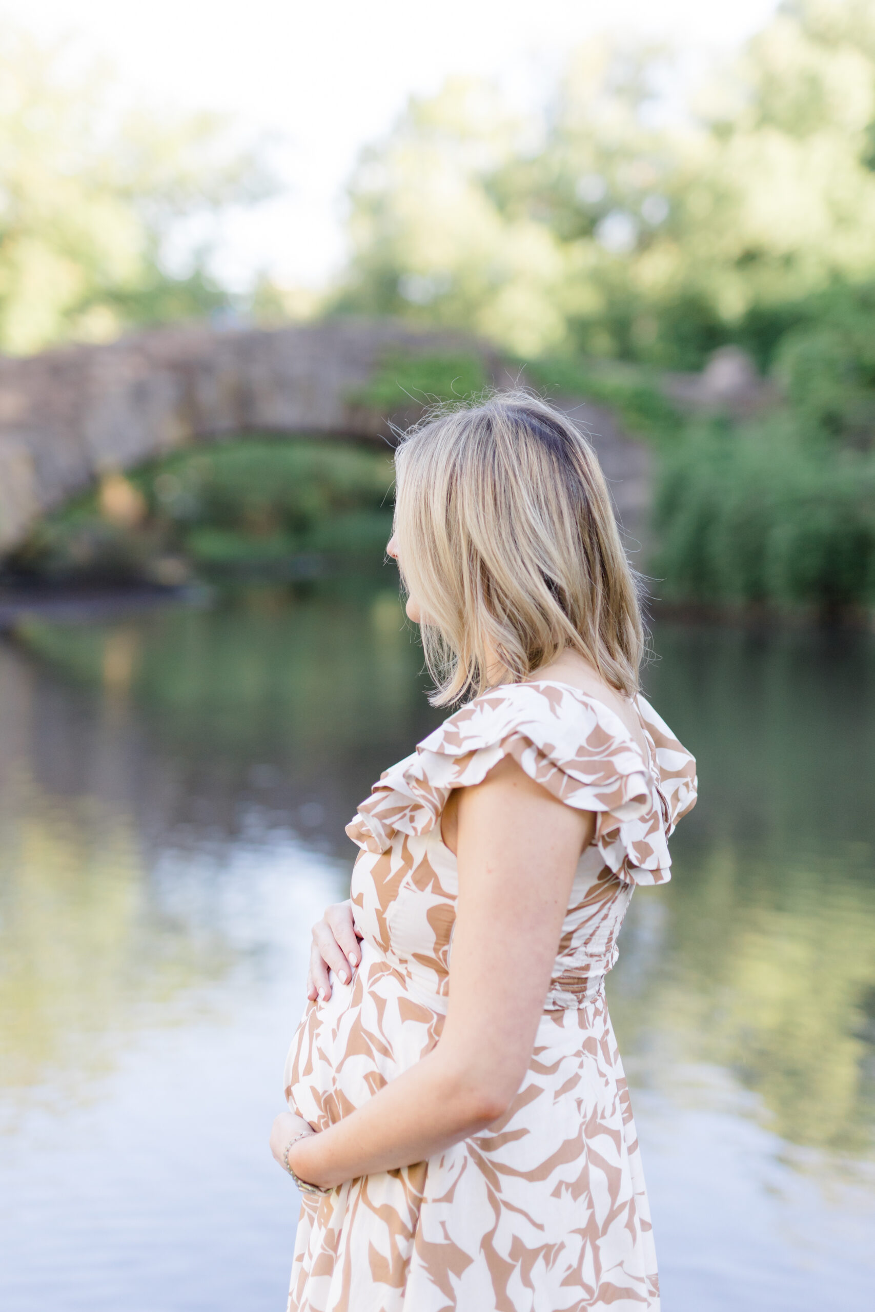 A pregnant woman looks out at the water at a maternity photo session in Central Park shot by Jacqueline Clair Photography