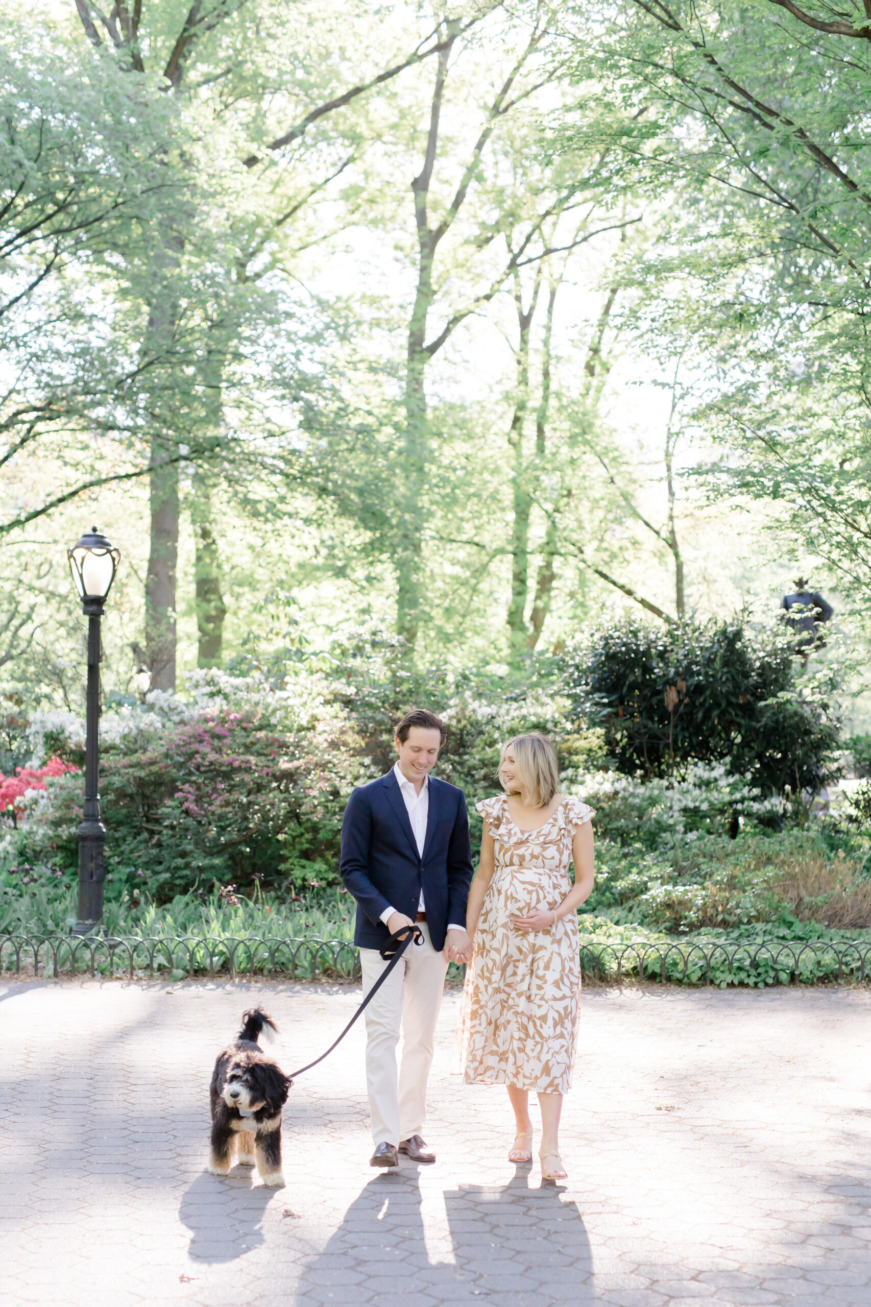An expecting mom and her husband walk with their dog at a maternity photo session in Central Park shot by Jacqueline Clair Photography