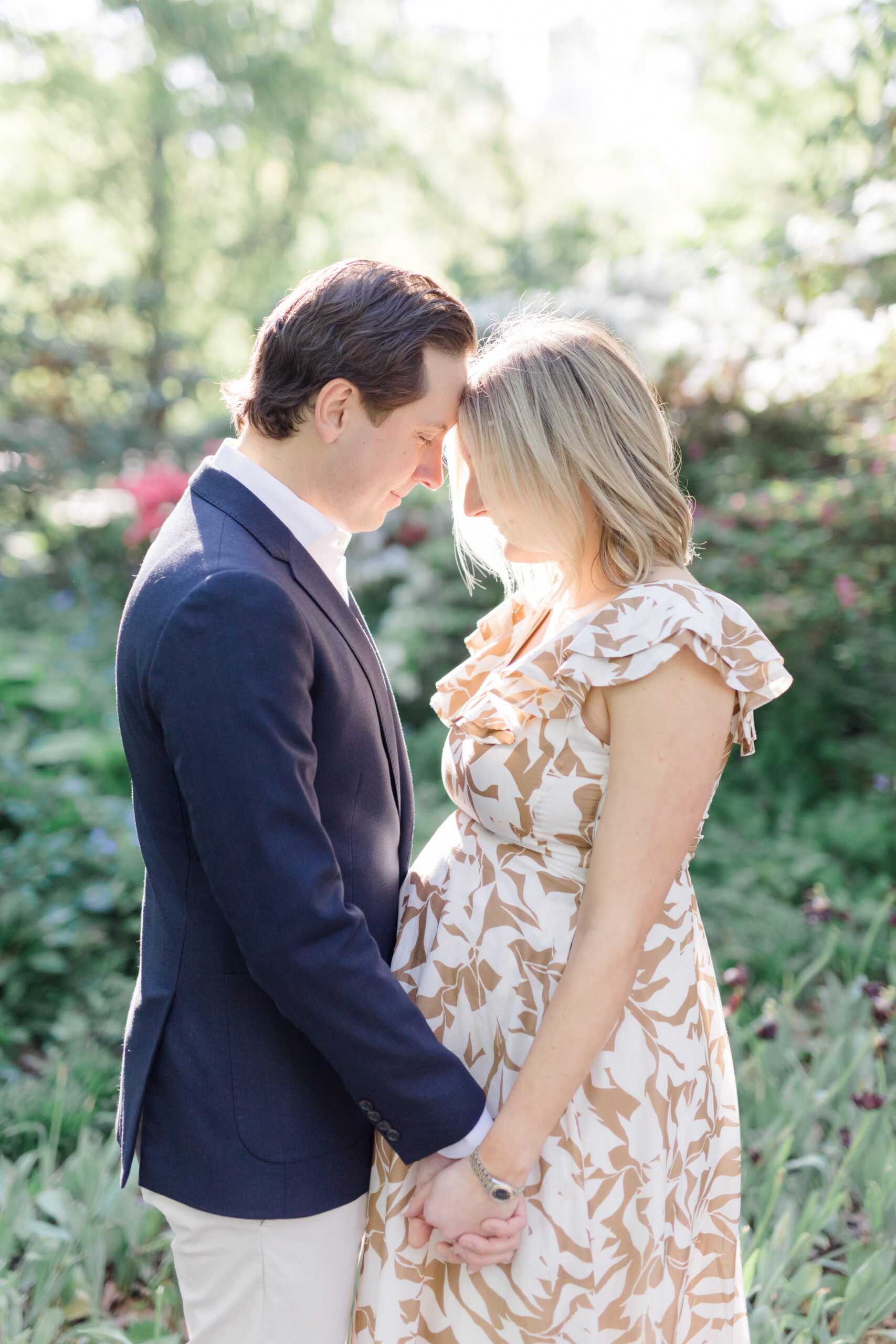 An expecting mom and her husband touch foreheads and hold hands at a maternity photo session in Central Park shot by Jacqueline Clair Photography