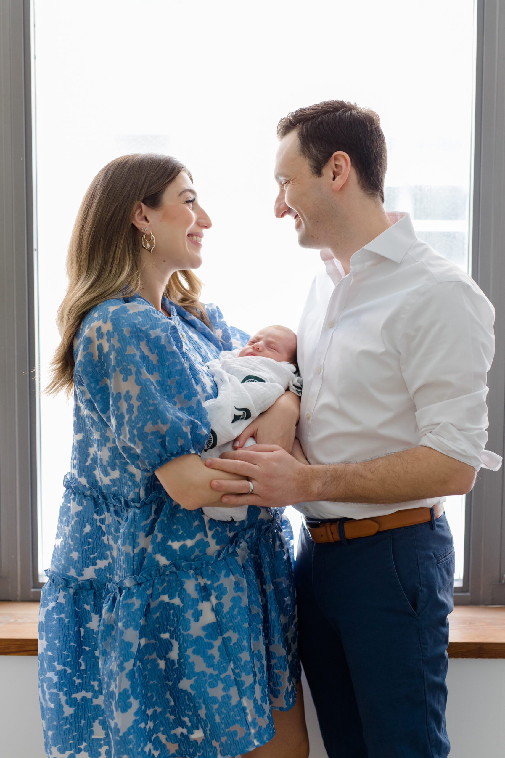 A mom ad dad smile at each other while holding their baby at a newborn session with New York City newborn photographer Jacqueline Clair