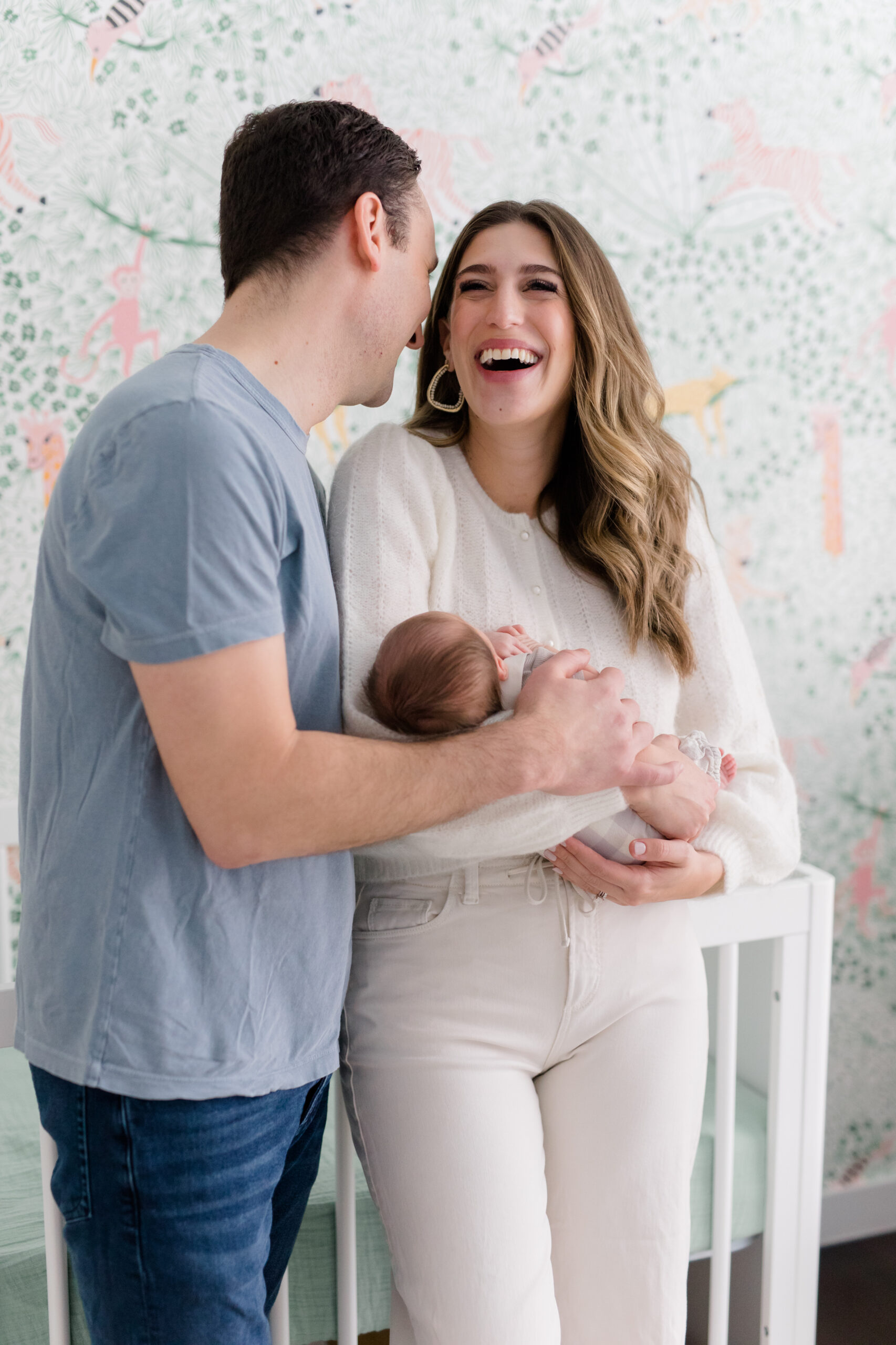 A mom and dad laugh while holding their baby at a newborn session with New York City newborn photographer Jacqueline Clair
