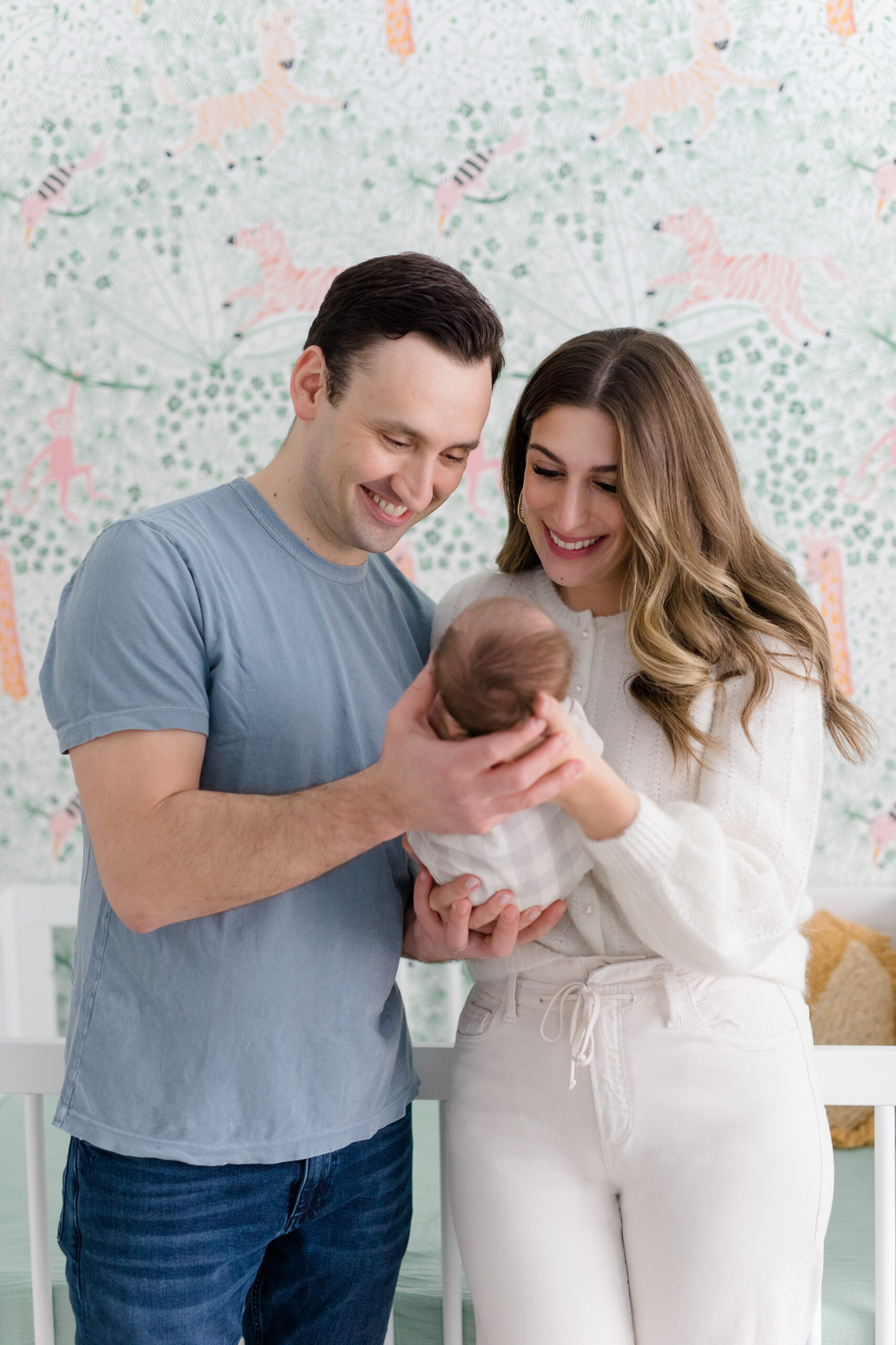 A mom and dad smile at their baby at a newborn session with New York City newborn photographer Jacqueline Clair