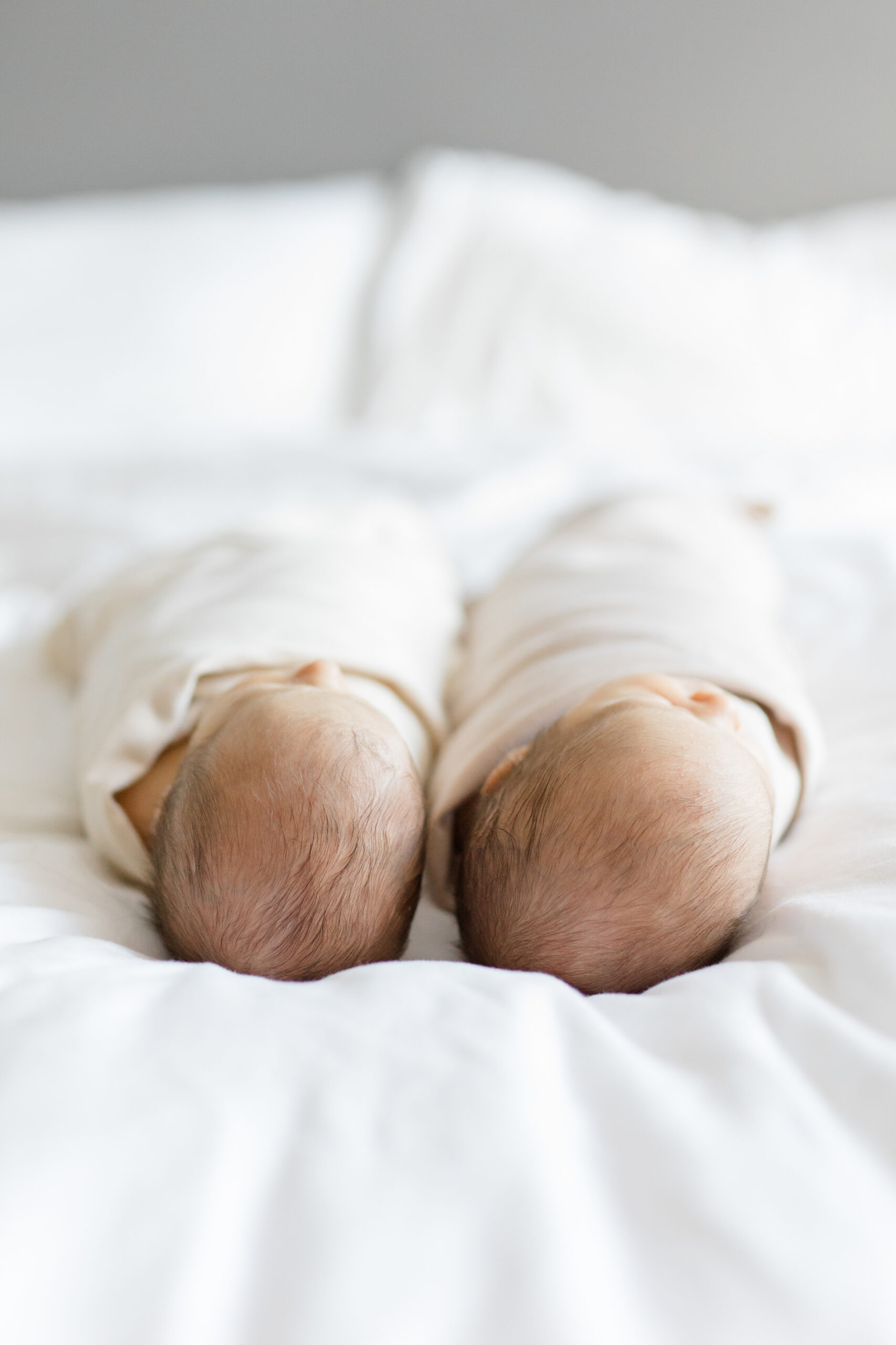 Twin babies lying next to each other on a bed at a twin newborn photography session with Jacqueline Clair Photography