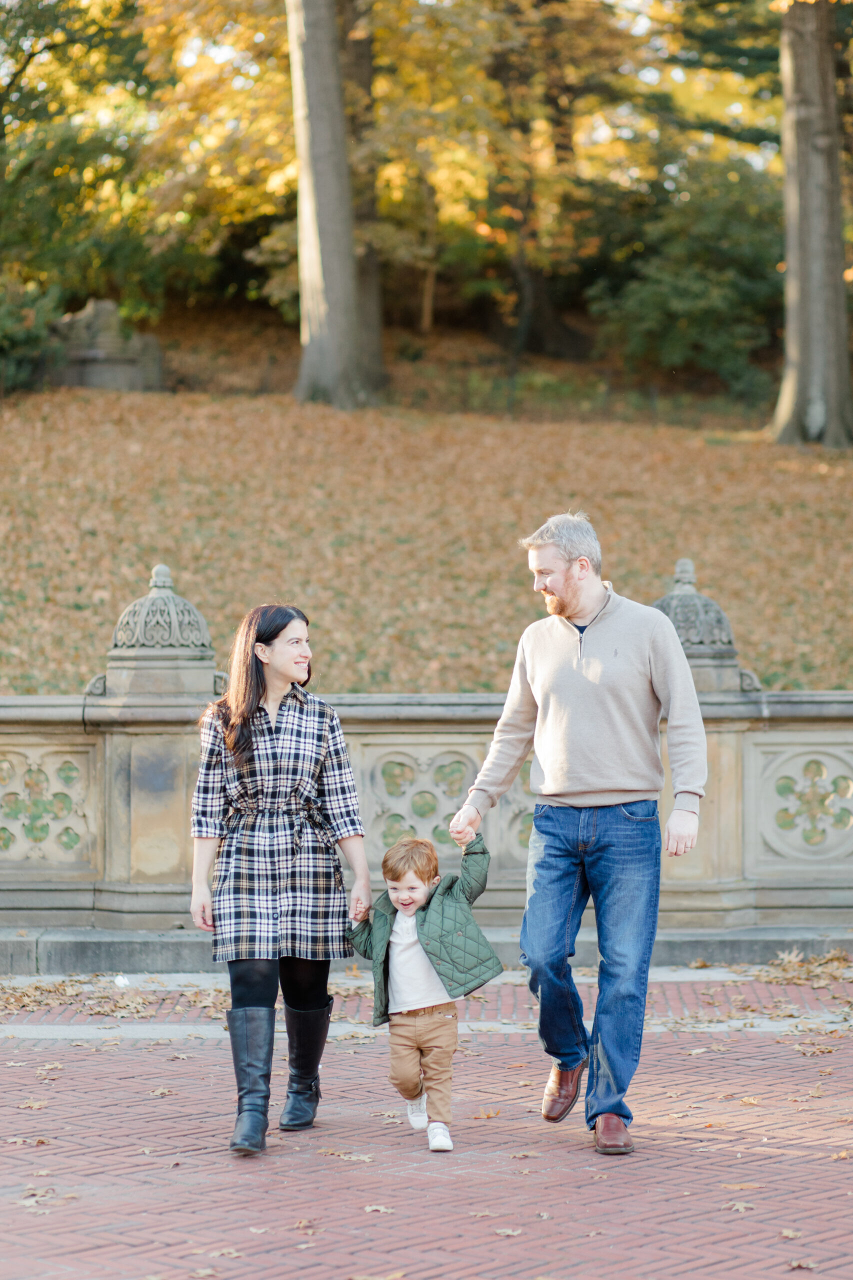 A mom, dad, and their young son walk together in Central Park at a fall family session photographed by Jacqueline Clair Photography