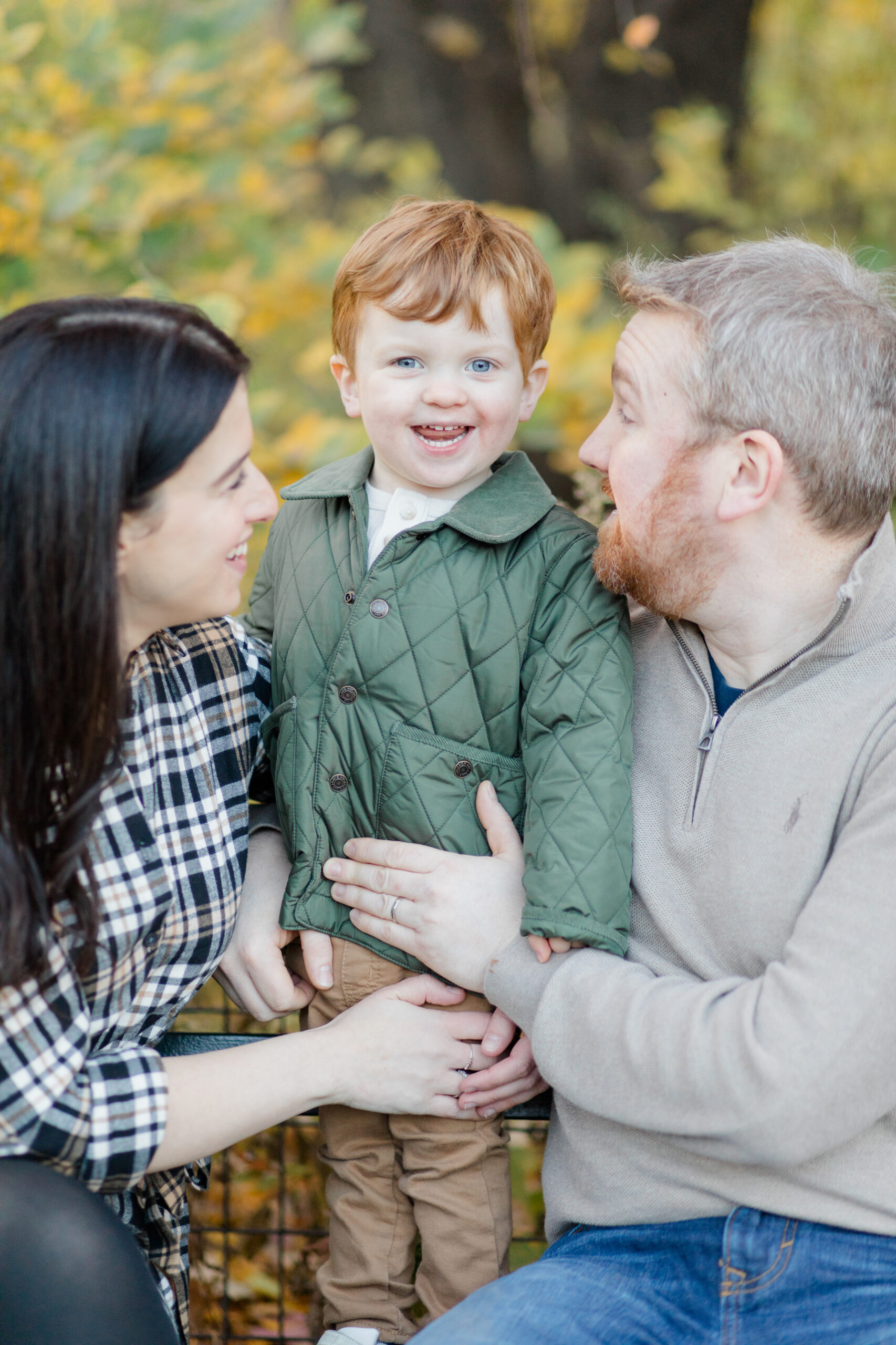 A little boy grins with his mom and dad at a fall family session photographed by Jacqueline Clair Photography