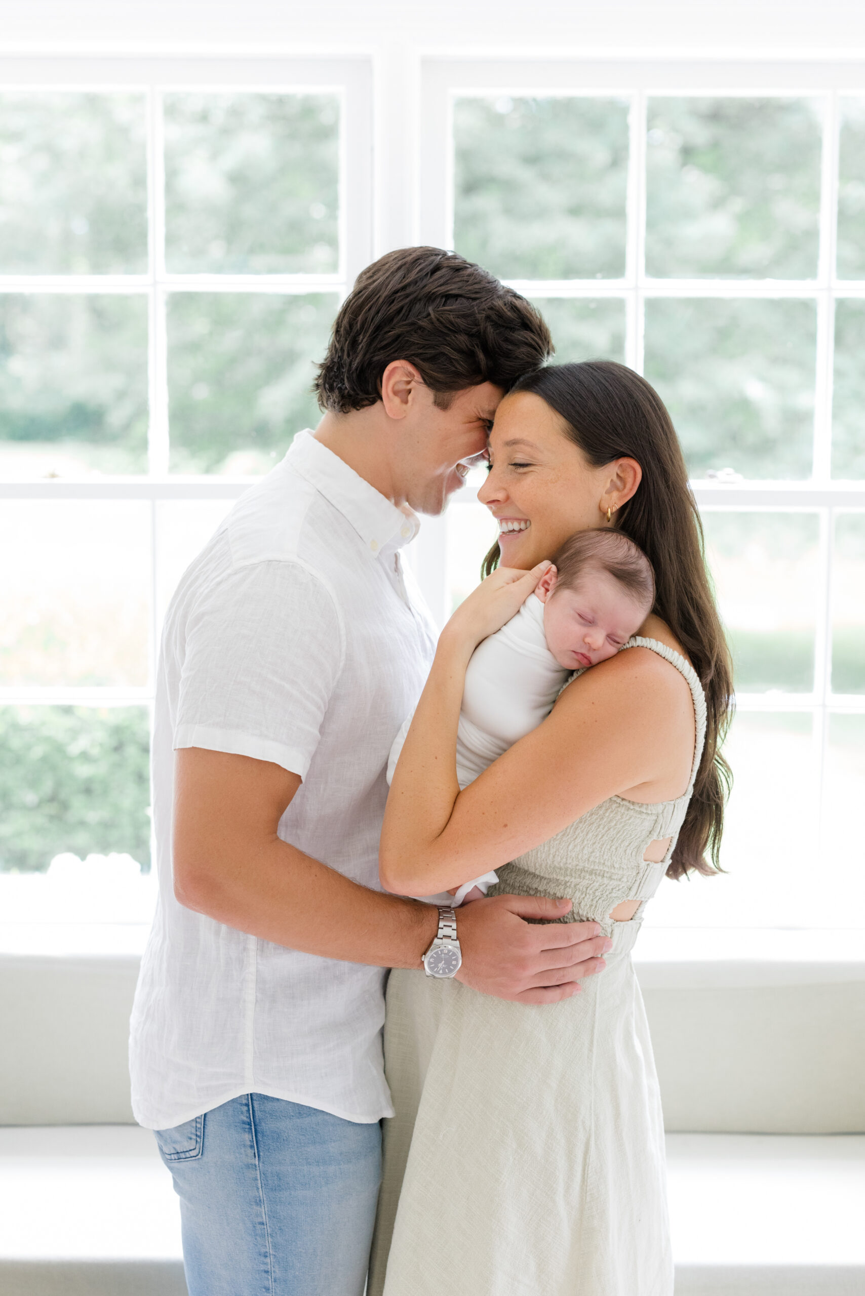 A man wearing jeans and a white button down and his wife wearing a light green dress at their lifestyle newborn session