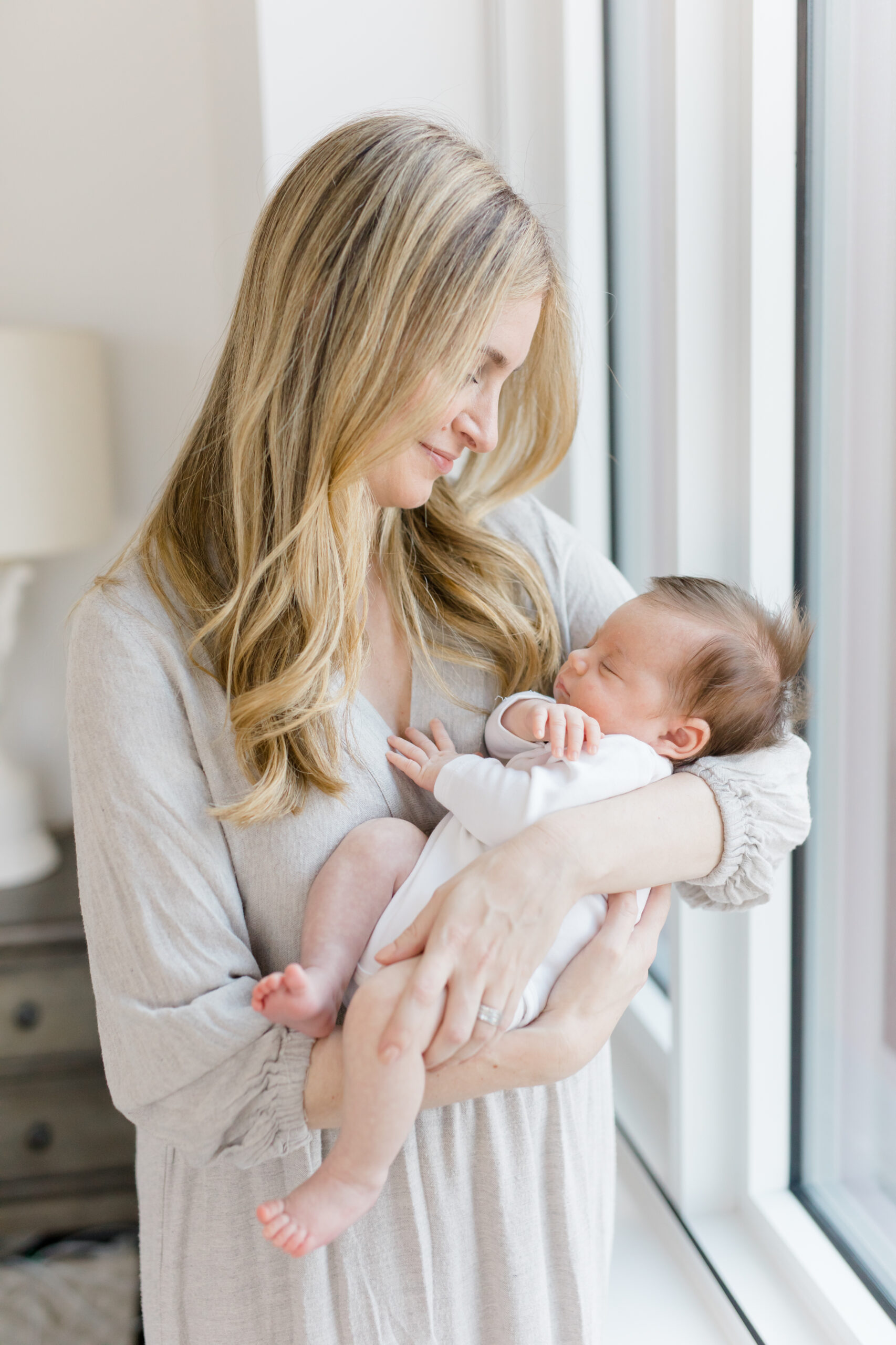 A mom wears a neutral beige dress and holds her baby