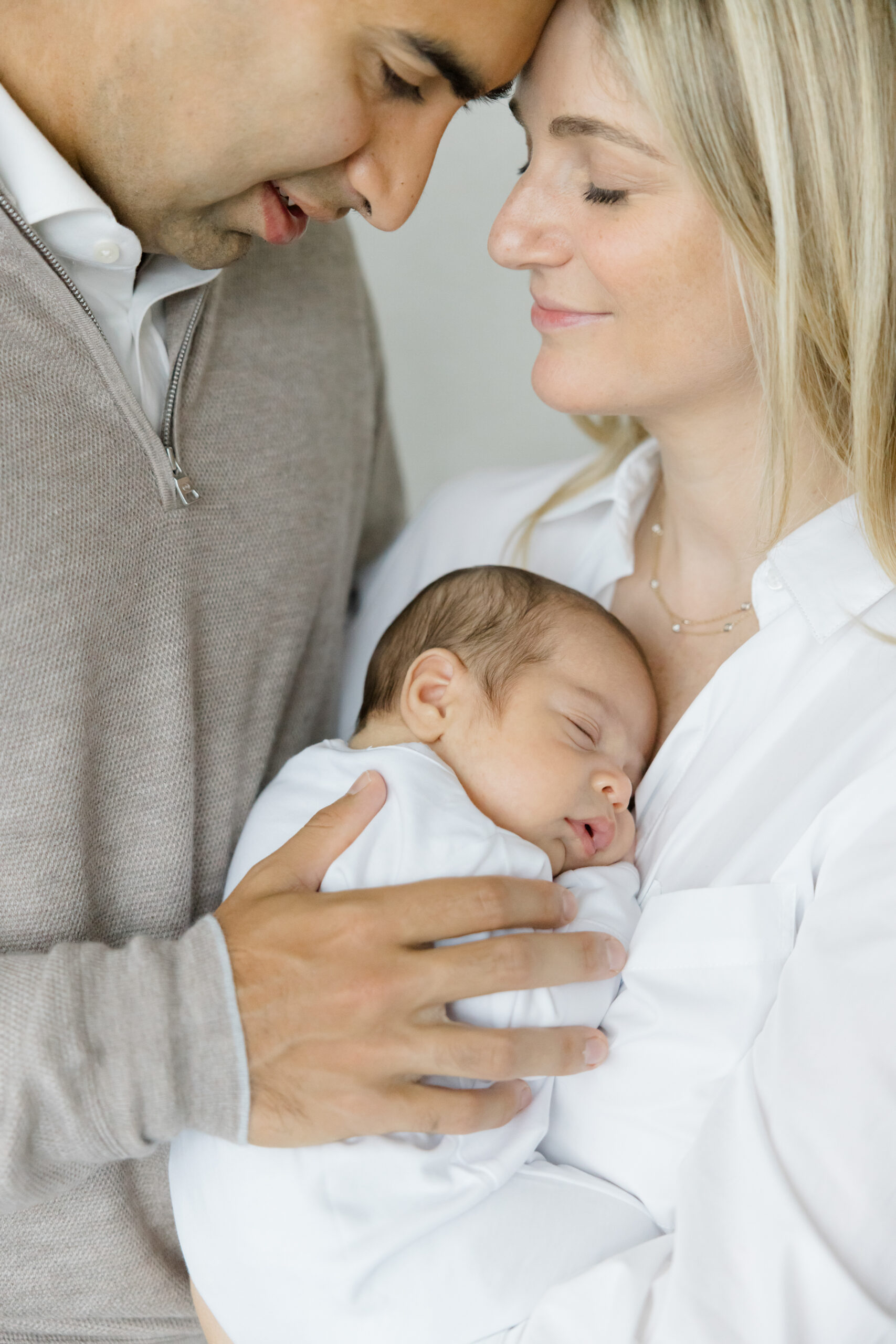 A husband and wife dressed in white and light beige-brown for their lifestyle newborn session