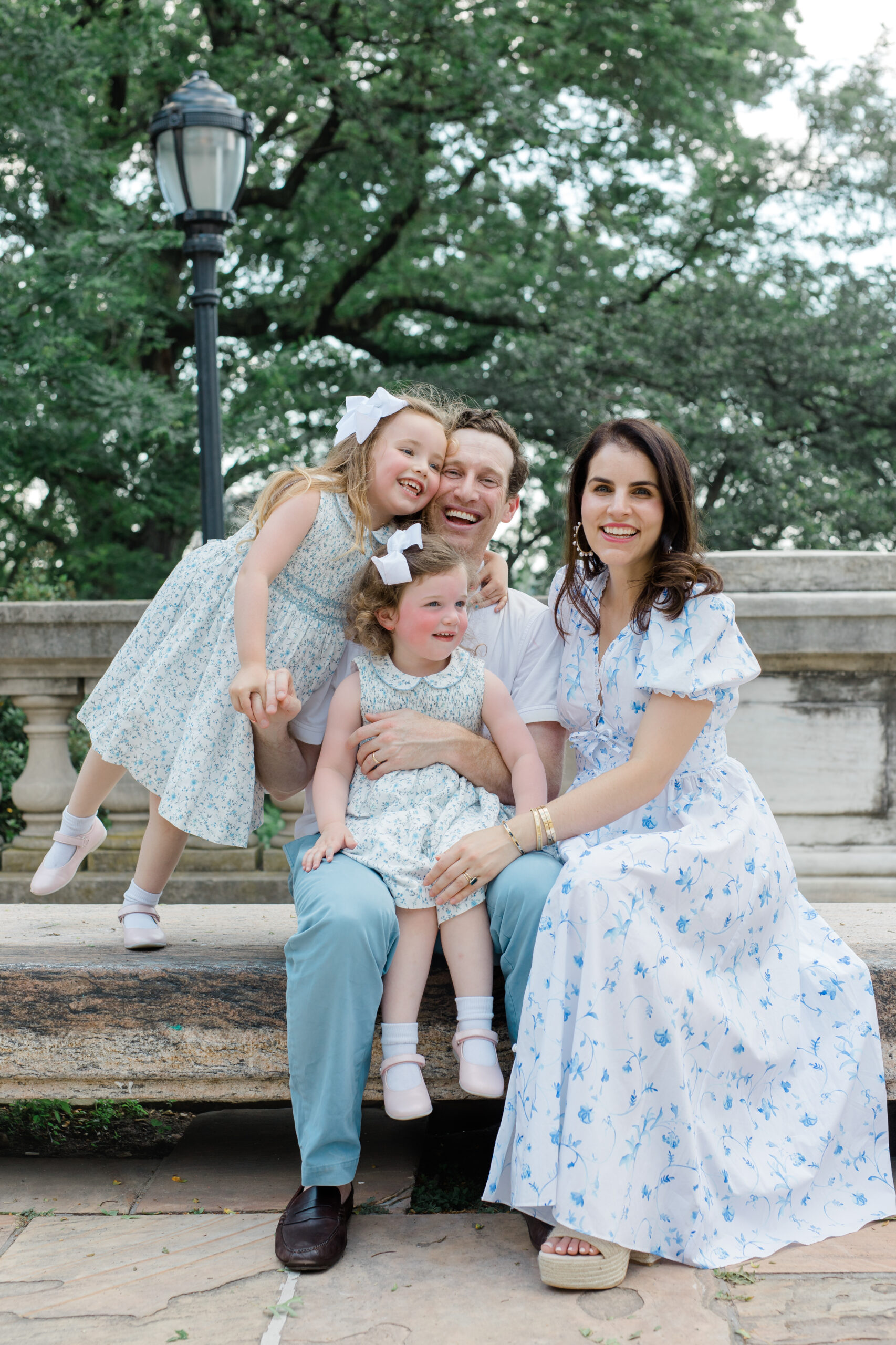 A family of dad, mom, and two young daughters wear shades of white and blue as an example of what to wear for spring family photos. 